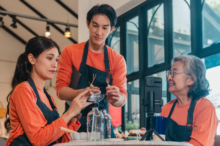 A mother, son, and daughter from a family business host a live stream, showcasing ceramic products on camera while managing orders and engagement for e commerce sales.の写真素材