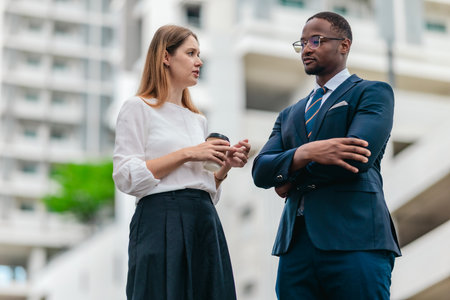 Two business leaders hold a focused corporate discussion outside a modern office complex, conveying CEO-level conversation, leadership, and decision-making in an urban setting.の写真素材