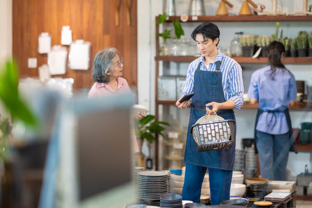 A senior woman shops for tableware while a couple who own the family ceramic store assist her with...