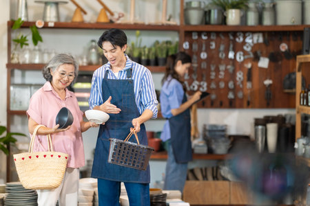 A senior woman shops for tableware while a couple who own the family ceramic store assist her with...