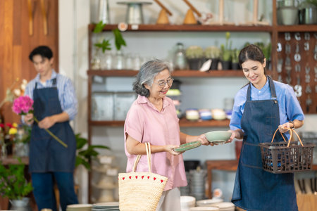 A senior woman shops for tableware while a couple who own the family ceramic store assist her with product selection and service at the boutique.の写真素材