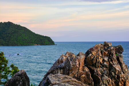 A scenery of sea at the sunset time with a rock and leaves at the bottom and a mountain at a side of a photo in Chantgaburi Thailand.の写真素材