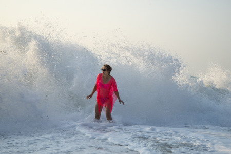 A wave of two meters surprises a young woman on the seashore/ A young woman caught by a big wave /Moment of impact between a huge wave and a young woman/ A moment a young woman is taken by a huge waveの写真素材