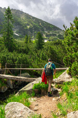 Photography of a male hiker in the mountains approaching a wooden bridge over a creek. Still of a hiker in the mountains crossing on a bridgeの写真素材