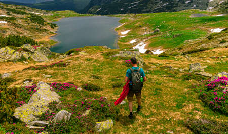 Photography of a male hiker in the mountains admiring a beautiful lake down in the valley in summer time with cloudy weather.の写真素材