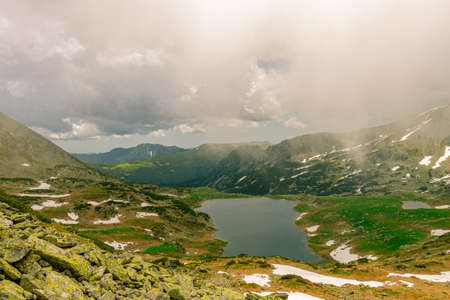 Beautiful view of a glacial lake in the mountains under cloudy sky. View of Bucura lake located in Retezat mountains in Romania. View of a mountain lake in a rainy day.の写真素材
