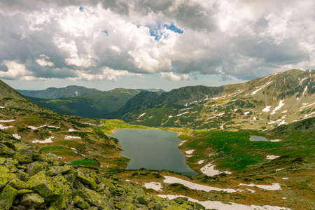 Beautiful view of a glacial lake in the mountains under cloudy sky. View of Bucura lake located in Retezat mountains in Romania. View of a mountain lake in a rainy day.の写真素材