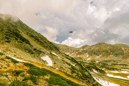 Photography of a small drone hovering above the ground in a mountain enviroment.  Still of a small droneの写真素材