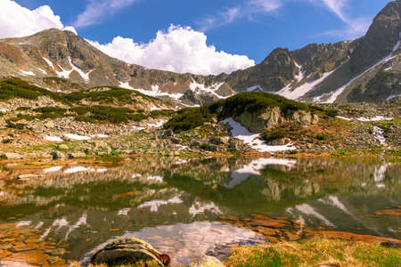 Lovely landscape photography of a mountain lake with mountain peaks in the background. Weather is sunny with a couple pf clouds. Glacial lake in the mountains landscape in summerの写真素材