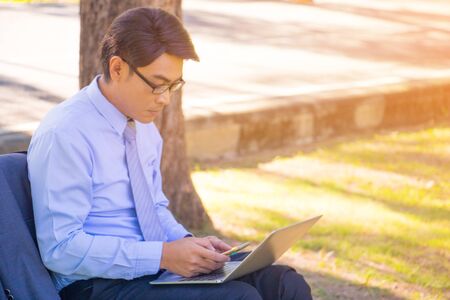 Business man,He is sitting on bench in park.He is play notebook and  thinking about business.He is search internet and  relax time.Photo concept  business and relax time.の写真素材