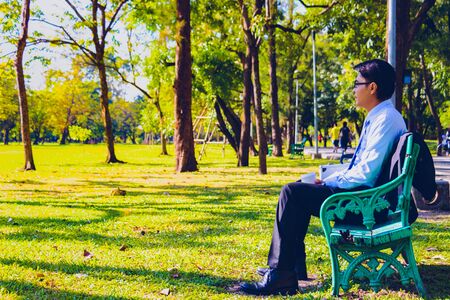 Business man,He is sitting on bench in park.He is thinking about business. He is drinking coffee beside business bag.Photo concept  business and relax time.の写真素材