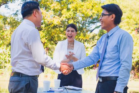 Business man handing a contract agreement and after a deal between business success.Business women clapping nice and smile.They are happy beside stream in park.Photo concept business and succeed.の写真素材