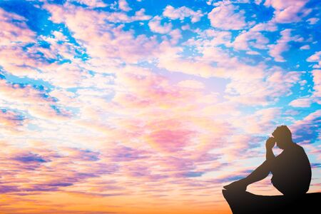 Silhouetted photo. Lonely man  sitting on cliff.He is unhappy and sad.He is watching the evening glow.Photo concept for Silhouetted and depression.の写真素材