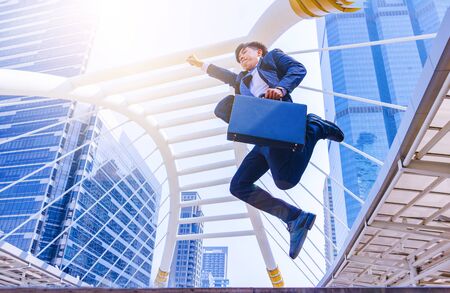 A young Asian businessman in town. A man jump in to sky. He is happy and gleeful. Portrait, Handsome, Bangkok, Thailand. Photo businessman and good feel concept.の写真素材