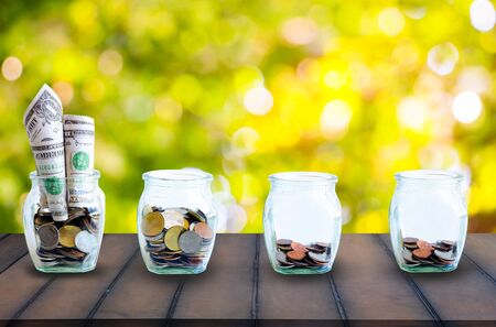 The coins in bottle on sky background. The ray sun on  the coins in the bottle on old wood. The concept of growth for the save money.の写真素材