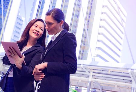 Businesswoman in town.They are use tablet and talking on walkway. She  holding tablet and talking with partner. Photo concept team work and Business.の写真素材