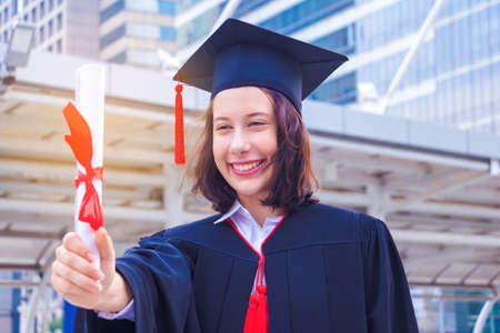 She is  Graduate and wearing  graduate's dress.She standing and show degree certificate.She is celebration education graduation.She is happy in good time.Photo concept  Education and success.の写真素材