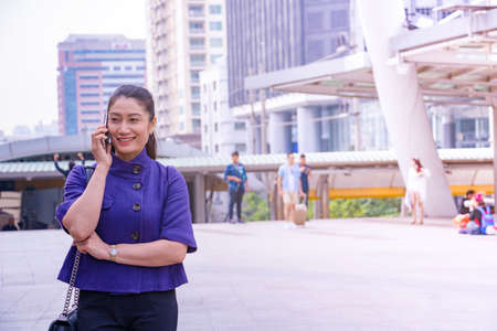 Woman use smart phone on walkway. She  is standing and call phone.She is smile and happy. Photo concept technology for work and slow life.の写真素材