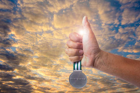 A hand and A golden medal. Hand is holding and the hand is putting the gold medal up the dark sky. Meaning of golden medal instead of winner and successful Photo concept Success and win.の写真素材