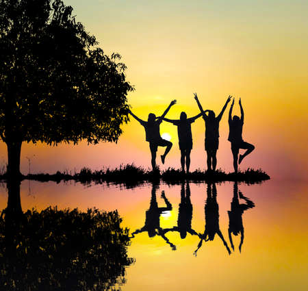Silhouetted and reflection in still water sunset background.They are standing with tree and show hand together.They are enjoying and watching the evening glow together. Photo concept for Silhouette.の写真素材