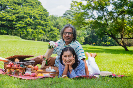 Young Asian in park. they are having a picnic and relax time.A man sent apple for woman. She is  lying on the grass beside picnic basket. Photo lifestyle and picnic idea.の写真素材