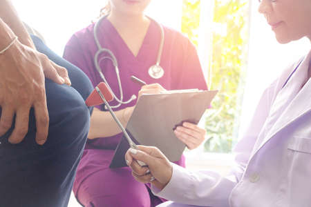 Close â up doctor and male patient.Doctor using  examining patient  knee jerk reflex with nurse  note it. patellar reflex,take care,Photo concept medicine and health care.の写真素材