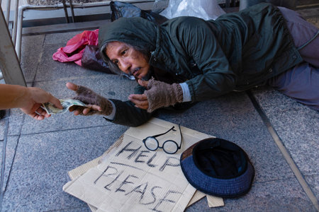 Homeless man is sitting down on walkway in town. He is receive dollar.He is  hoping to have the better life. poverty, despair, Photo Sympathetic and hope concept.の写真素材