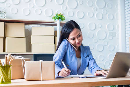 The young  Asia Businesswoman.She is writing and use mobile phone. She makes it for order online. She is happy and smiles. Gift , Business, Photo concept work and Shopping.の写真素材