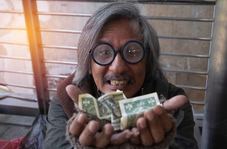 Homeless man is sitting down on walkway in town.He is receive dollar.He is hoping to have the better life. poverty, despair, Photo Sympathetic and hope concept.の写真素材