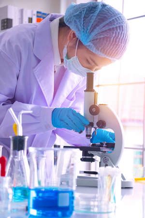 Young Asia  woman scientist working in laboratory.She is looking microscope.She is trying and research with red and blue test tube. Experiment , chemical Photo concept develop and medicine.の写真素材