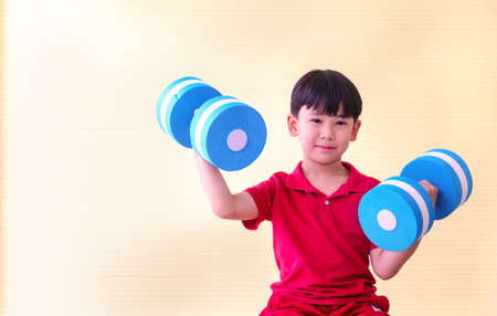 Portrait Asian cute  boy. He is sitting with Dumbbell.He is action in room.Child boy raise dumbbell.photo concept freedom  and  Kid portrait.の写真素材