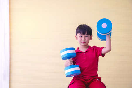 Portrait Asian cute  boy. He is sitting with Dumbbell.He is action in room.Child boy raise dumbbell.photo concept freedom  and  Kid portrait.の写真素材
