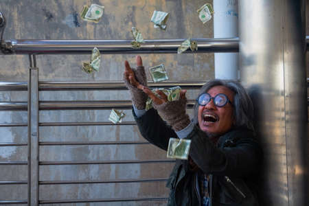 Homeless man is sitting down on walkway in town. He is receive dollar.He is very glad and happy. poverty, despair, Photo Sympathetic and hope concept.の写真素材