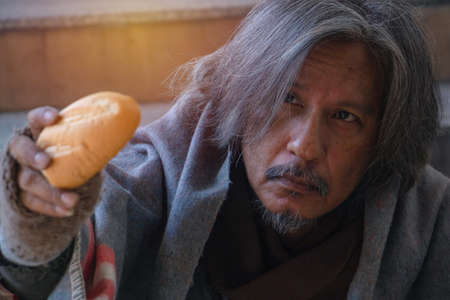 Homeless man is sitting down on staircase and walkway in town.He is Show bread.He is very unhappy. focus is face. poverty,despair, Photo Sympathetic and hope concept.の写真素材