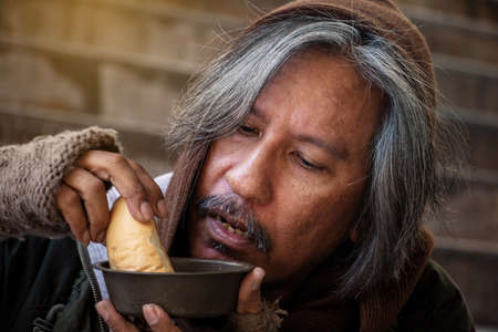 Homeless man is sitting down on staircase in town.He is eat bread and milk.He is very hungry and unhappy.poverty,despair, Photo Sympathetic and hope concept.の写真素材