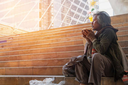Homeless man is sitting down on staircase in town.He is eat bread and milk.He is very hungry and unhappy.poverty,despair, Photo Sympathetic and hope concept.の写真素材