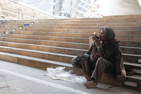 Homeless man is sitting down on staircase in town.He is eat bread and milk.He is very hungry and unhappy.poverty,despair, Photo Sympathetic and hope concept.の写真素材