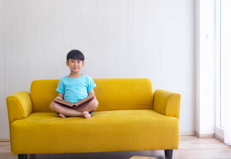 Portrait Asian cute boy.Child boy sitting and read red books.He is sitting  on Yellow sofa in room.lovely,nice, development.photo concept knowledge and  Kid portrait.の写真素材