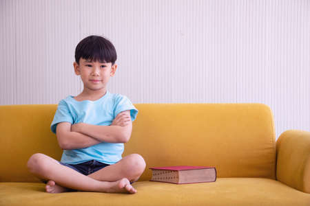 Portrait Asian cute boy.Child boy sitting and read red books.He is sitting  on Yellow sofa in room.lovely,nice, development.photo concept knowledge and  Kid portrait.の写真素材