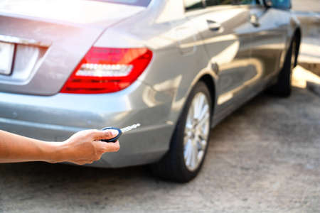 The hand woman holding a car key and back of a woman carrying a shopping bag with the car in the background. They returned from shopping.buy,sell,Photo concept Lifestyle and Shopping.の写真素材
