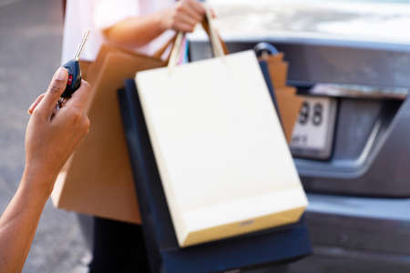 The hand woman holding a car key and back of a woman carrying a shopping bag with the car in the background. They returned from shopping.buy,sell,Photo concept Lifestyle and Shopping.の写真素材