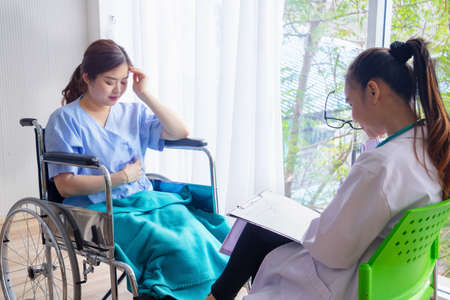 Doctor with female patient in hospital.Doctor giving a consultation woman about illness to a female patient sitting on wheelchair,Asian doctor woman,depression.Photo concept Health and Patient.の写真素材