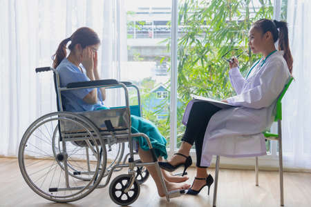 Doctor with female patient in hospital.Doctor giving a consultation woman about illness to a female patient sitting on wheelchair,Asian doctor woman,depression.Photo concept Health and Patient.の写真素材