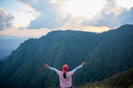 Women standing on cliff and see over view in nature.She is raise hand up and enjoying fresh air.She enjoying free happiness in beautiful Thailand landscape.photo concept active and nature background.の写真素材