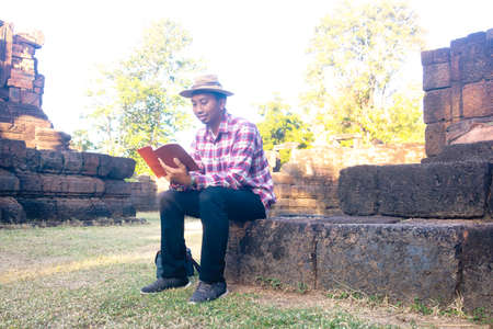 Asian man sitting under big tree and reading book.he is reading book and relaxing time in public park. learning day,clever,intelligent,Photo vacations and Lifestyle concept ideaの写真素材