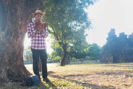 Asian man sitting under big tree and reading book.he is reading book and relaxing time in public...