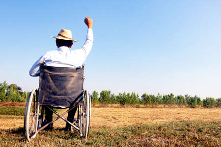 Young disabled man with field background.He is sitting on wheelchair and raising hand  up

.He is looking into sky.despair,lonely,hope.Photo concept depression and Patient.の写真素材