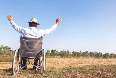 Young disabled man with field background.He is sitting on wheelchair and raising hand  up

.He is looking into sky.despair,lonely,hope.Photo concept depression and Patient.の写真素材
