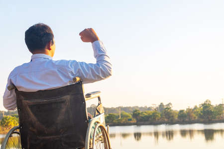 Young disabled man with field background.He is wearing a hat and sitting on wheelchair.He is looking...