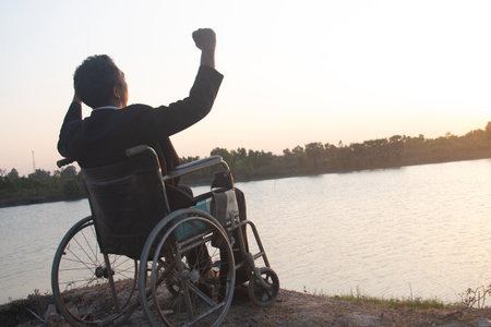Silhouette young disabled man seeing river background.He is raise a hand to and sitting on wheelchair.Photo concept depression and Patient.despair,lonely,hope.Photo concept depression and Patient.の写真素材